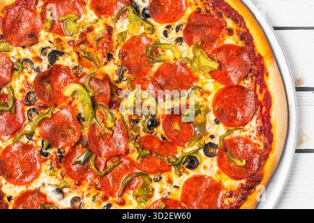 Vue aérienne d'une pizza pepperoni avec poivrons verts et olives noires sur un plateau métallique. Banque D'Images