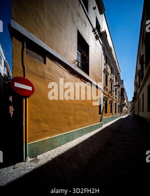 La lumière du soleil méditerranéen illumine les murs ocres de l'étroite rue García Ramos à Séville, créant de forts contrastes et des ombres profondes. Banque D'Images