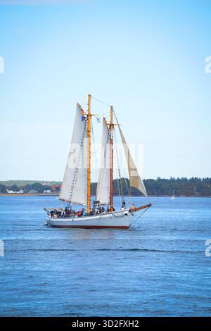 Une goélette à deux mâts glisse sur une eau bleue calme avec des voiles levées, offrant une vue sereine sur la vie maritime et la beauté de la voile côtière. Banque D'Images