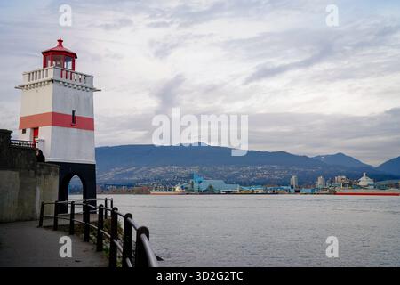 Le phare de Brockton point se dresse au-dessus de la digue dans le parc Stanley, face au port et aux montagnes de North Shore sous un ciel couvert. Banque D'Images