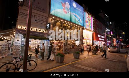 BUSAN, CORÉE DU SUD - 10 OCTOBRE. 2025 - les acheteurs passent devant des magasins éclairés et des enseignes au néon dans une rue animée la nuit Banque D'Images