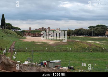 Vaste arène romaine ancienne en herbe avec clôtures, une cabane de chantier et des ouvriers sous un ciel nuageux, Circo Massimo, Rome, Italie Banque D'Images