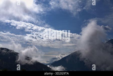 Les nuages dérivent à travers les vallées de montagne sous un ciel bleu vif, révélant des couches de lumière et d'ombre à travers le paysage alpin accidenté. Banque D'Images