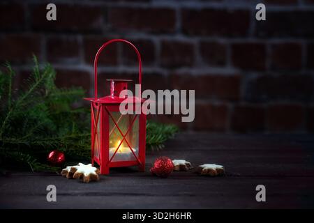 Petite lanterne rouge avec bougie allumée et quelques décorations de Noël contre un mur de briques, lumière dans le patio pendant la saison sombre, espace copie, sélectionné Banque D'Images