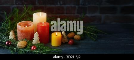 Quatre bougies orange et rouge avec décoration de Noël contre un mur de briques foncées, grand format panoramique, concept pour les vacances, l'Avent ou le nouvel an, copie Banque D'Images