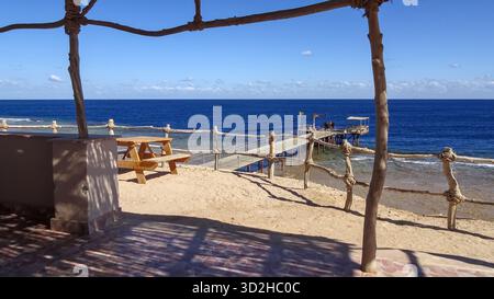 Vue depuis un coin salon confortable près de la plage dans un petit hôtel au bord de la mer Rouge, regardant vers une courte jetée qui s'étend sur le plat de récif peu profond Banque D'Images