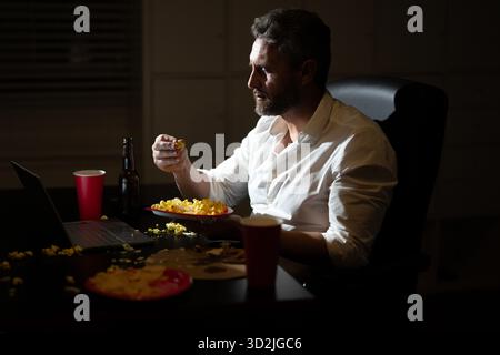 Homme d'affaires manger de la pizza en heures supplémentaires. Homme occupé mangeant le dîner et travaillant en ligne au bureau de nuit. Entrepreneur millénaire travaille tard dans la nuit tout en profitant Banque D'Images