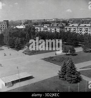 Archive photo noir et blanc de Sloviansk, Ukraine, juillet 1997. Cette vue à angle élevé montre la place centrale de la ville - la place de la Révolution d'octobre (maintenant place Soborna). La photo capture la grande place ouverte, un parc (skver) avec des ruelles, des sapins et des parterres de fleurs. Une petite scène est au premier plan. En arrière-plan, la place est encadrée par des bâtiments résidentiels 'Stalinka' (période Staline). Cette image capture une journée d'été paisible dans une ville post-soviétique. Banque D'Images