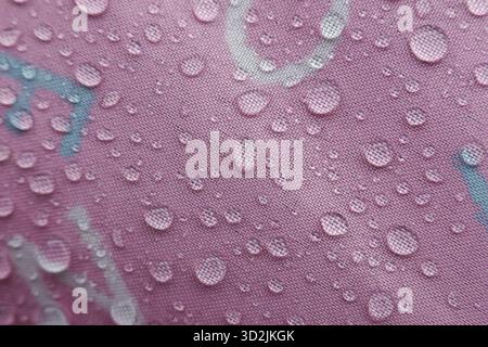 Des gouttelettes d'eau rafraîchissantes s'accrochent à la surface rose éclatante, mettant en valeur une texture fascinante et une belle résilience de matériau imperméable après des s doux Banque D'Images