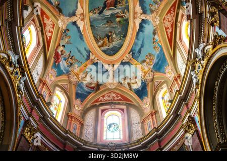 Mdina, Malte - 2025 : magnifique plafond d'une ancienne église baroque avec fresques religieuses vives, vitraux voûtés, détail doré Banque D'Images