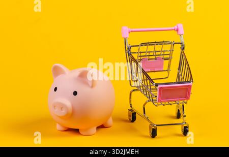 Chariot de magasinage avec tirelire en gros plan sur fond jaune Banque D'Images