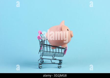 Chariot de magasinage avec tirelire en gros plan sur fond bleu Banque D'Images