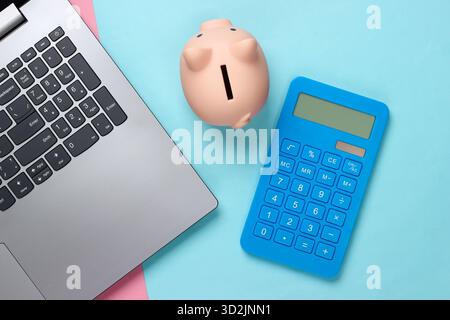 Ordinateur portable avec tirelire, calculatrice sur fond pastel bleu rose. Prise de vue minimaliste en studio. Vue de dessus. Pose à plat. Banque D'Images