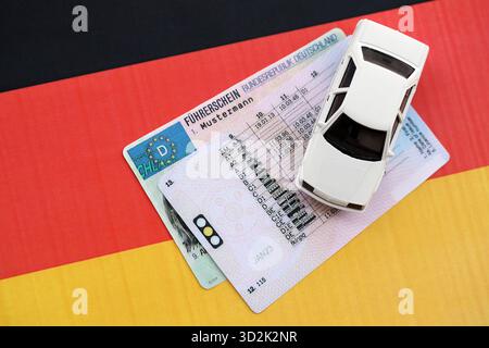 Carte de permis de conduire allemand appelé Fuhrerschein avec voiture jouet se trouve sur le drapeau allemand de près Banque D'Images