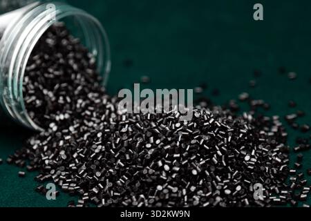 Capsules de kératine. Capsules noires de kératine. Granulés de plastique noir renversés de pot sur fond vert. Photo de haute qualité Banque D'Images