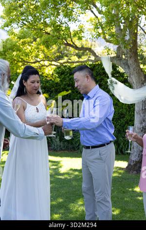 Célébration en plein air, toast de groupe senior diversifié avec champagne lors du mariage dans le jardin. Personnes âgées, célébration, diversité, rassemblement, joie, bonheur || autorisation du modèle Banque D'Images