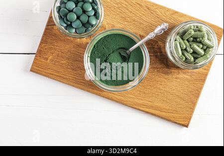 Poudre de spiruline verte, comprimés ronds, capsules dans divers bols en verre et bocaux sur un support en bois. Vue de dessus. Un super complément alimentaire Banque D'Images