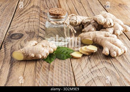 Bouteille avec bouchon en liège avec huile essentielle naturelle de racine de gingembre sur la racine d'une grande plante sur une table en bois. Concept de préparation de l'huile à la maison Banque D'Images