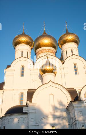 Plan vertical en bas angle d'une façade blanche d'église orthodoxe russe avec plusieurs dômes en oignon doré scintillant sur un ciel bleu clair Banque D'Images