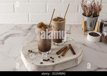 Deux grands verres avec une boisson au chocolat ou du café froid avec du lait et des glaçons se tiennent sur un podium en bois en face d'un mur de briques blanches Banque D'Images
