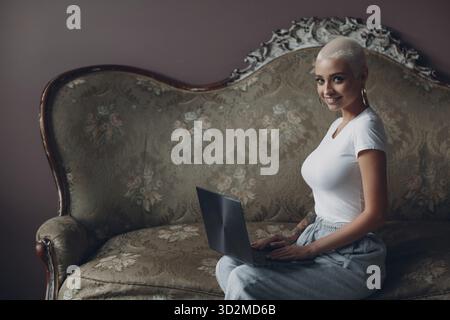 Coacher une jeune femme d'affaires avec un petit portrait de cheveux blond assis et souriant avec un ordinateur portable sur un canapé vintage et regardant l'appareil photo Banque D'Images