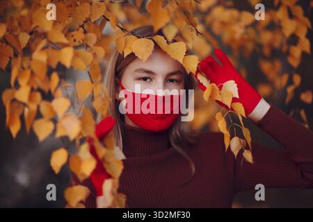 Jeune femme active en gants rouges et masque facial à parc d'automne Banque D'Images