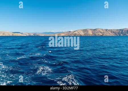 Vue sur l'océan serein avec des montagnes lointaines sous un ciel bleu clair. Banque D'Images