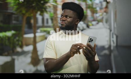 L'homme tape le smartphone avec le doigt tout en plissant devant l'écran dans une rue animée de la ville, les mains visibles et l'écran du téléphone tenu près ; légère gêne. Banque D'Images