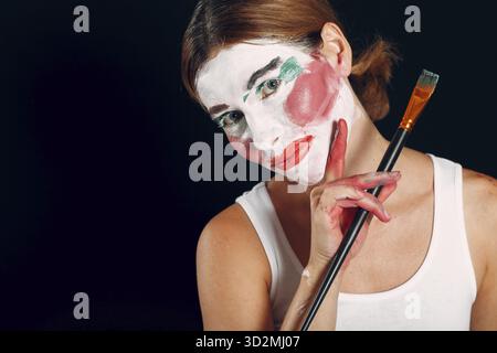 Jeune femme appliquant le maquillage, peint le visage avec pinceau et maquillage. Comment ne pas faire le clown de cirque de concept de maquillage Banque D'Images