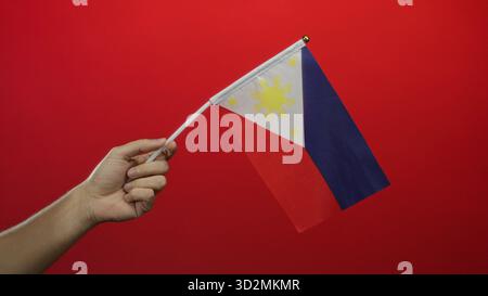 Homme tenant le drapeau philippin sur un fond rouge avec une focalisation isolée mettant en valeur le patriotisme et la fierté nationale. Banque D'Images