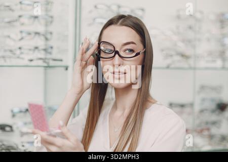 Jeune belle mannequin femme avec des lunettes pour le maquillage en opticien. Femme souriante dans des lunettes pour le maquillage Banque D'Images