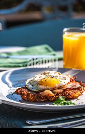 Petit déjeuner au soleil avec cappuccino, rosti de pommes de terre avec oeuf frit et bacon et jus d'orange, sur fond vert, vertical Banque D'Images