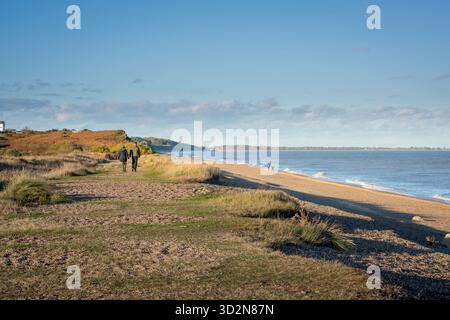 Couple plage UK, vue arrière de deux jeunes marchant ensemble à côté de la plage à Dunwich dans le Suffolk, Angleterre, Royaume-Uni. Banque D'Images