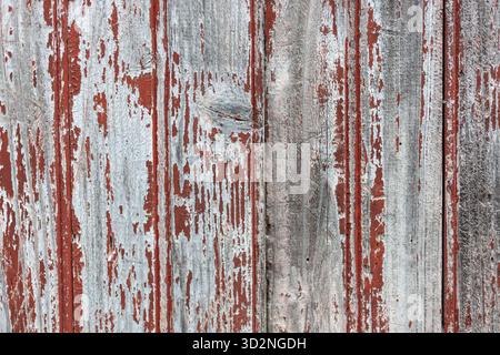 Gros plan de planches de bois altérées avec de la peinture rouge fanée sur un mur rustique de grange. Banque D'Images