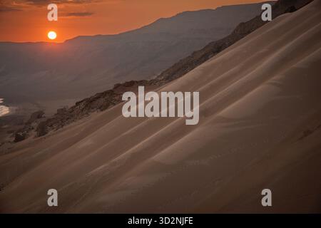 Un beau coucher de soleil peint le ciel de couleurs chaudes tandis que les dunes et les montagnes s'élèvent le long de la côte de Socotra, au Yémen, créant une scène sereine. Banque D'Images
