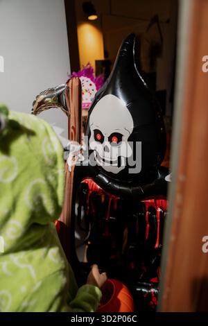 Halloween rencontre de l'enfant dans le costume de pyjama de dinosaure rencontrant la décoration gonflable sinistre faucheuse avec le visage de crâne et les yeux rougeoyants pendant le voisin Banque D'Images