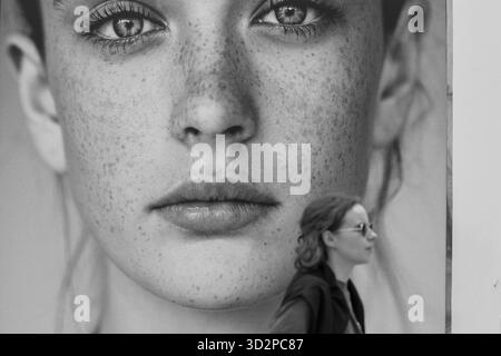 Braga, 14 juin 2025 - Une femme promène des pâtes sur un grand panneau d'affichage portrait dans une rue de la ville, capturé en noir i nwhite Banque D'Images