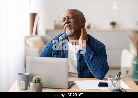 Homme africain senior éprouvant des douleurs au cou tout en travaillant dans un cadre de bureau moderne Banque D'Images