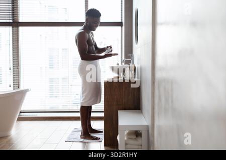 Black Man aime la routine de rasage tout en restant debout dans la salle de bain moderne Banque D'Images
