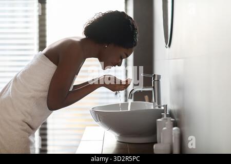 Young Black Lady effectue la routine de soins de la peau du matin dans une salle de bains élégante Banque D'Images