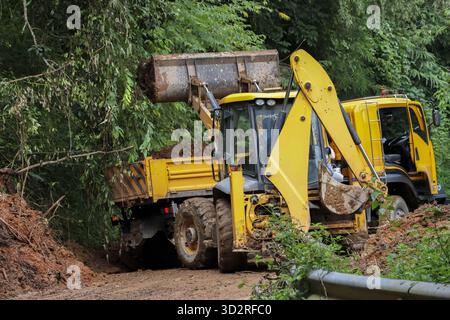 Chargeuse-pelleteuse jaune pour enlever la saleté et le sol de la route rurale, charger les débris dans le camion à benne basculante. Machinerie lourde sur le chantier de construction dans la nature, creuser Banque D'Images