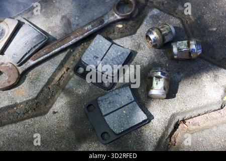 Scène de réparation automobile ciblée avec de vieilles pièces de voiture rouillées. Les plaquettes de frein neuves, les écrous de roue et la clé sont posés sur une surface métallique sale lorsque le véhicule est difficile Banque D'Images