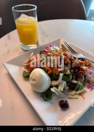 Un repas nutritif sur une assiette blanche, avec une salade colorée avec un œuf dur, des légumes frais, des légumes rôtis, des trempettes et un verre d'orange j Banque D'Images