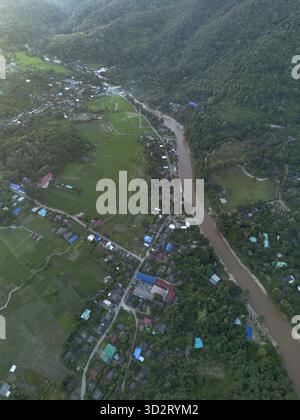 La vue aérienne révèle un village rural tranquille niché paisiblement par une rivière sinueuse. Entouré par un paysage de montagne verdoyant, la beauté de la nature abonde, Banque D'Images