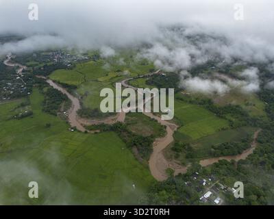 Le paysage aérien capture une rivière boueuse sinueuse qui coule gracieusement à travers une vallée verdoyante et un champ fertile. Environnement naturel, partiellement voilé Banque D'Images
