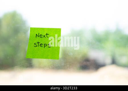 Note adhésive verte sur une fenêtre affichant les étapes suivantes comme rappel pour la planification future Banque D'Images