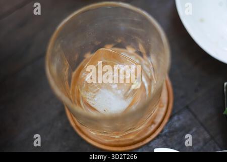 Verre vide solitaire avec glaçon fondu sur les dessous de verre après avoir fini la boisson. Une scène d'après-soirée montre un gobelet avec des résidus d'une boisson alcoolisée lik Banque D'Images
