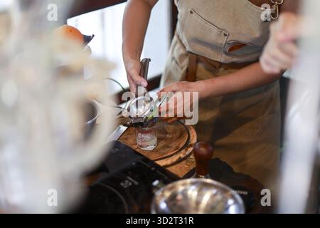 Femme concentrée pressant des agrumes frais dans la cuisine. Porter un tablier tout en préparant une recette maison avec centrifugeuse manuelle et ingrédient naturel pour Banque D'Images