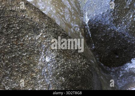 Gros plan puissant et serein de glace fondante coulant sur une formation rocheuse granitique rugueuse. Ce fond naturel abstrait montre la surface de pierre texturée w Banque D'Images