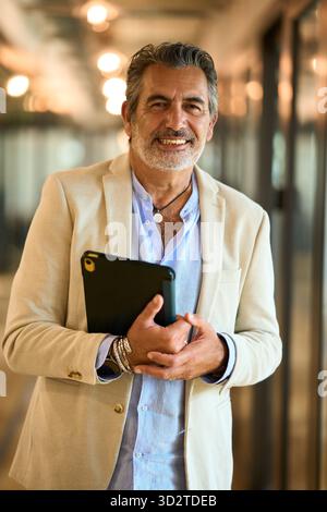 Homme d'affaires mature souriant, tenant la tablette dans le bureau Banque D'Images